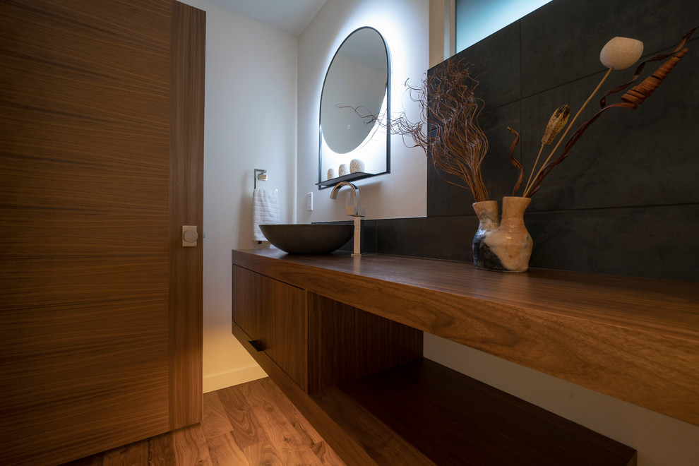 Gästetoilette mit offenen Schränken, Wandtoilette, schwarzen Fliesen, braunem Holzboden, Aufsatzwaschbecken und Waschtisch aus Holz in Seattle
