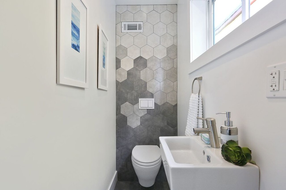 Foto på ett litet funkis toalett, med en toalettstol med hel cisternkåpa, grå kakel, skifferkakel, grå väggar och ett fristående handfat