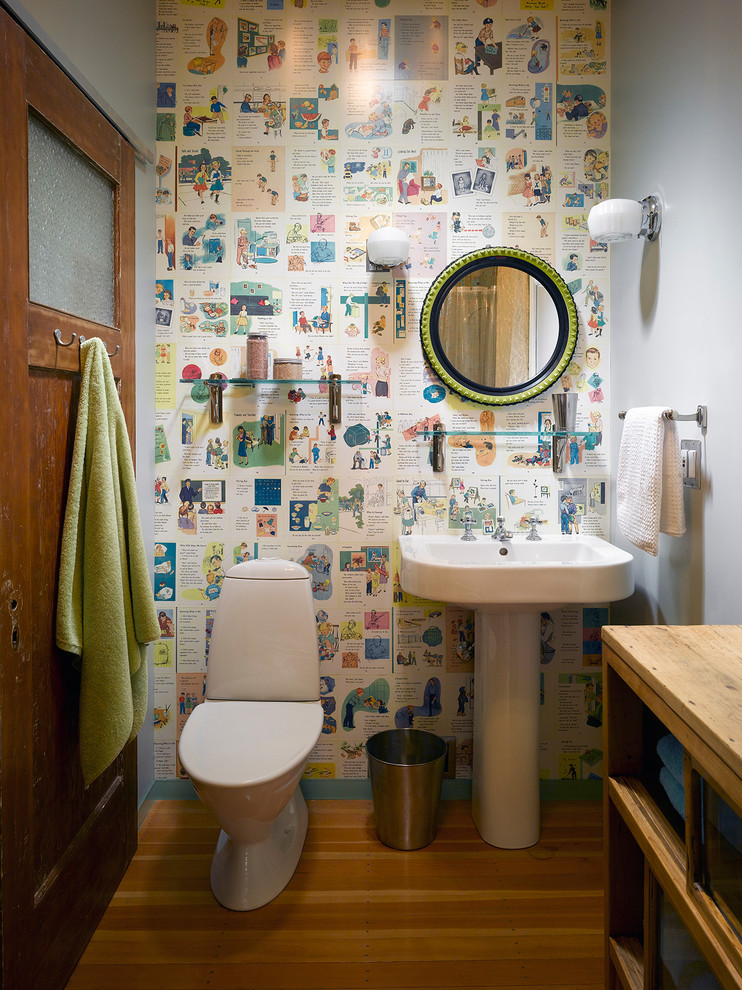 Eklektisk inredning av ett toalett, med en toalettstol med separat cisternkåpa, flerfärgade väggar, mellanmörkt trägolv och ett piedestal handfat