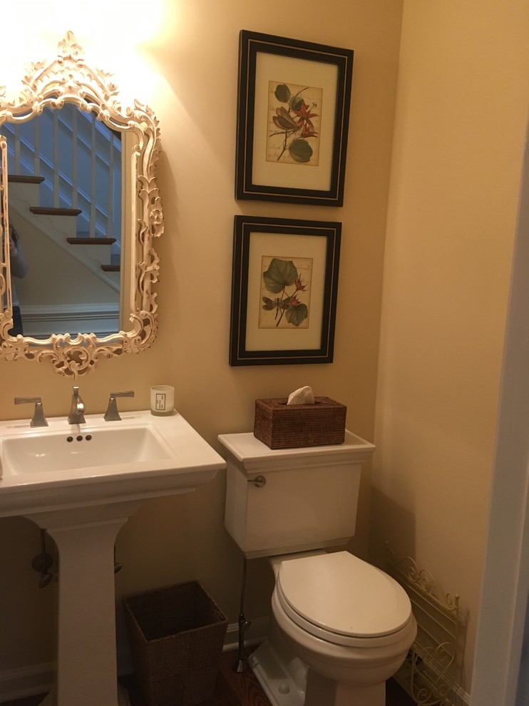 Kleine Klassische Gästetoilette mit Wandtoilette mit Spülkasten, gelber Wandfarbe, braunem Holzboden und Sockelwaschbecken in Philadelphia