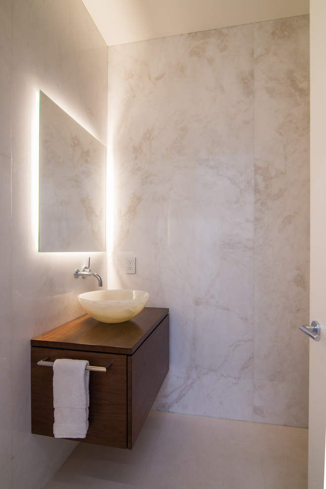 Example of a mid-sized trendy beige tile limestone floor and beige floor powder room design in Los Angeles with flat-panel cabinets, dark wood cabinets, beige walls, a vessel sink, wood countertops and brown countertops