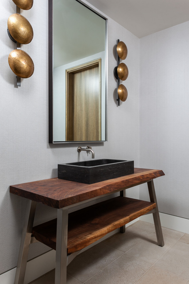 This is an example of a small contemporary cloakroom in Los Angeles with freestanding cabinets, dark wood cabinets, grey walls, limestone flooring, a vessel sink, wooden worktops and beige floors.