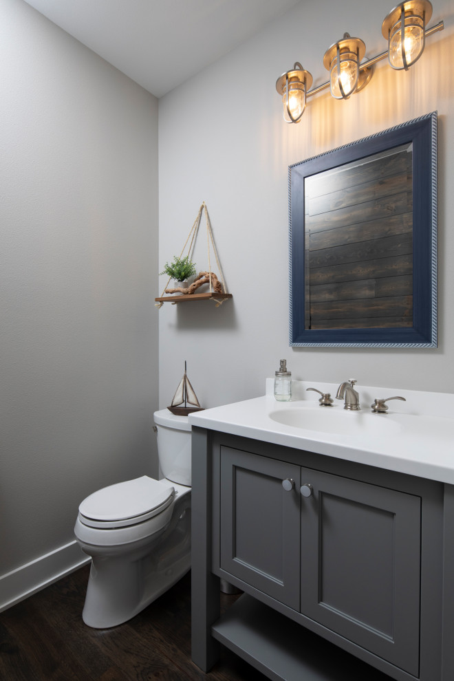 Inredning av ett amerikanskt litet vit vitt toalett, med möbel-liknande, grå skåp, en toalettstol med separat cisternkåpa, grå väggar, mörkt trägolv, ett integrerad handfat, bänkskiva i akrylsten och brunt golv