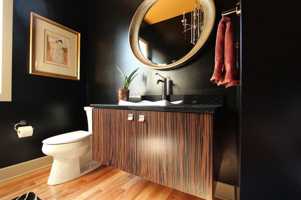 Inredning av ett eklektiskt mellanstort toalett, med släta luckor, skåp i mörkt trä, en toalettstol med separat cisternkåpa, svarta väggar, ljust trägolv, ett fristående handfat och bänkskiva i kvarts