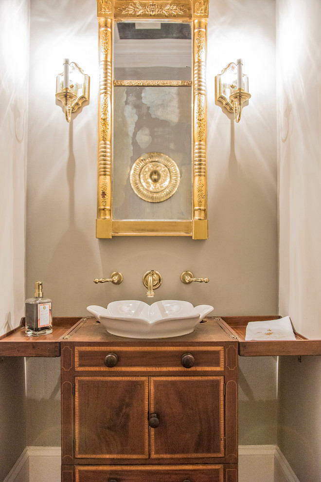 Klassisk inredning av ett litet toalett, med möbel-liknande, skåp i mörkt trä, en toalettstol med hel cisternkåpa, grå väggar, mellanmörkt trägolv, ett fristående handfat, träbänkskiva och brunt golv