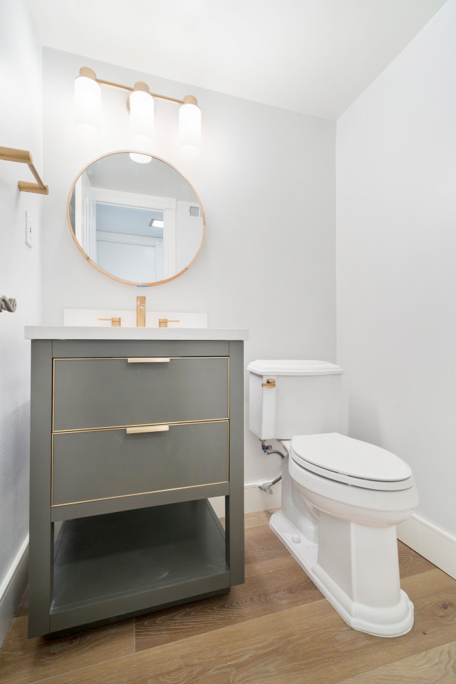 Пример оригинального дизайна: туалет в стиле неоклассика (современная классика) с серыми фасадами, серой плиткой, серыми стенами, полом из ламината, врезной раковиной, столешницей из искусственного кварца, коричневым полом и белой столешницей