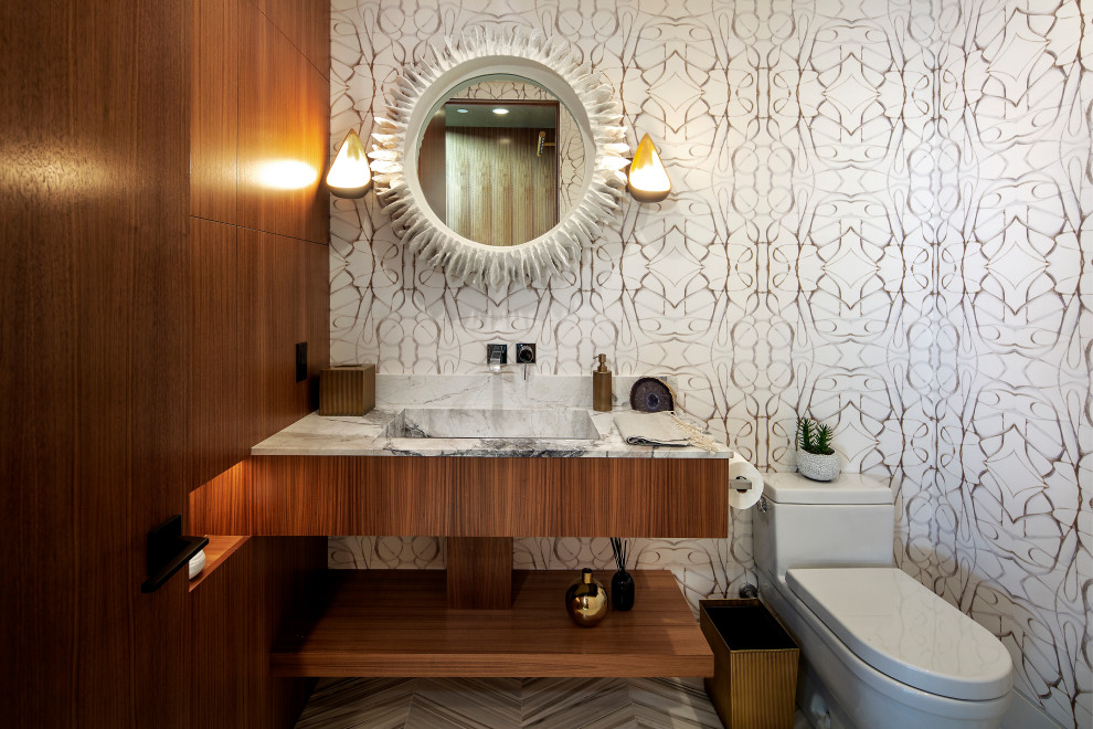 Moderne Gästetoilette mit flächenbündigen Schrankfronten, hellbraunen Holzschränken, weißer Wandfarbe, Quarzit-Waschtisch, weißer Waschtischplatte, Toilette mit Aufsatzspülkasten, integriertem Waschbecken und grauem Boden in Orange County