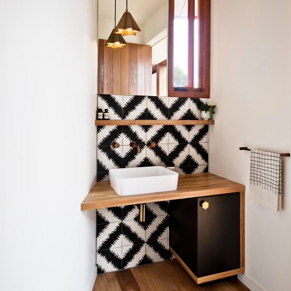 Moderne Gästetoilette mit Aufsatzwaschbecken, schwarzen Schränken, Waschtisch aus Holz, Zementfliesen, weißer Wandfarbe, braunem Holzboden, schwarz-weißen Fliesen und brauner Waschtischplatte in Melbourne