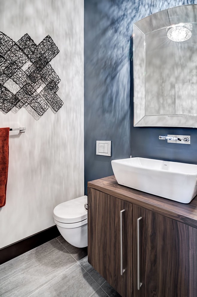 Idee per un bagno di servizio minimal di medie dimensioni con ante lisce, ante in legno bruno, WC sospeso, piastrelle grigie, piastrelle in ceramica, pareti blu, pavimento con piastrelle in ceramica, lavabo a bacinella e top in laminato