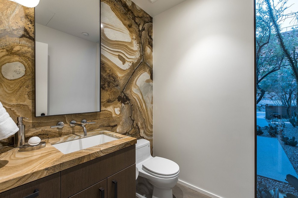 Inspiration for a medium sized contemporary cloakroom in Las Vegas with flat-panel cabinets, dark wood cabinets, a one-piece toilet, brown tiles, multi-coloured tiles, stone slabs, grey walls, a submerged sink, granite worktops and beige worktops.