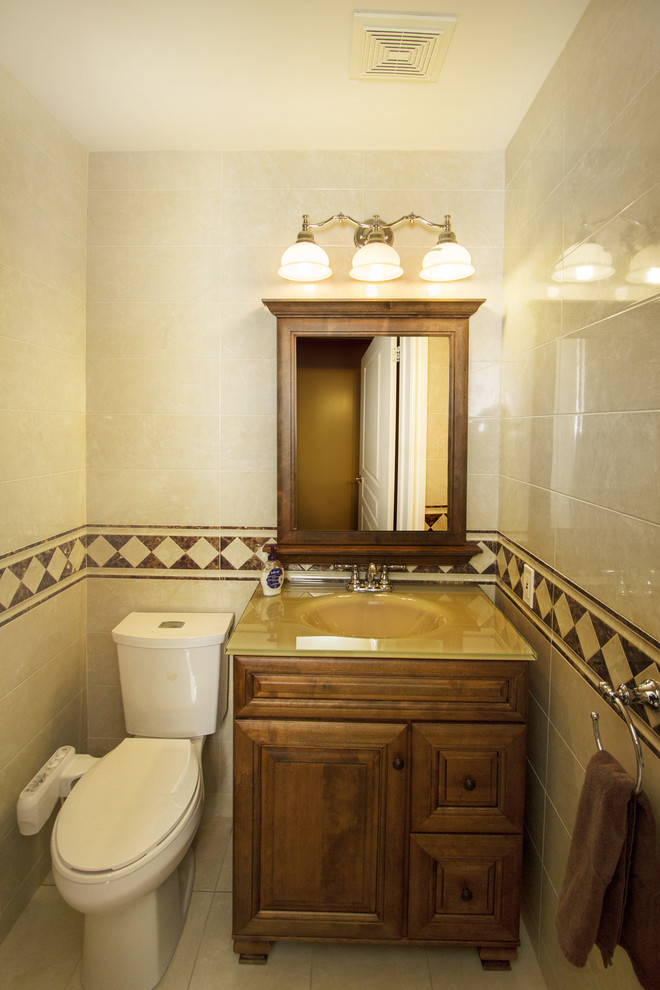 Réalisation d'un petit WC et toilettes design en bois brun avec un placard en trompe-l'oeil, WC à poser, un carrelage beige, des carreaux de porcelaine, un mur beige, un sol en carrelage de porcelaine, un lavabo intégré et un plan de toilette en verre.
