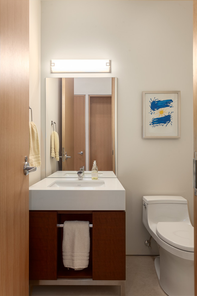 Immagine di un piccolo bagno di servizio moderno con ante lisce, ante in legno bruno, WC monopezzo, pareti beige, pavimento in pietra calcarea, top in quarzo composito e lavabo sottopiano