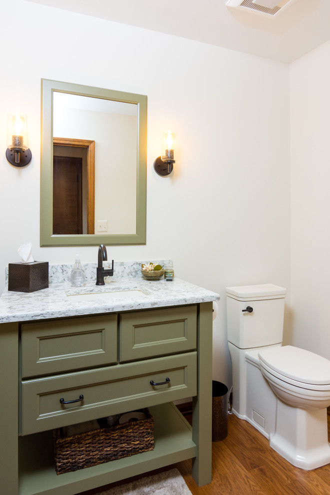 Inspiration for a mid-sized transitional medium tone wood floor and brown floor powder room remodel in Detroit with furniture-like cabinets, green cabinets, a two-piece toilet, white walls, an undermount sink, quartzite countertops and gray countertops