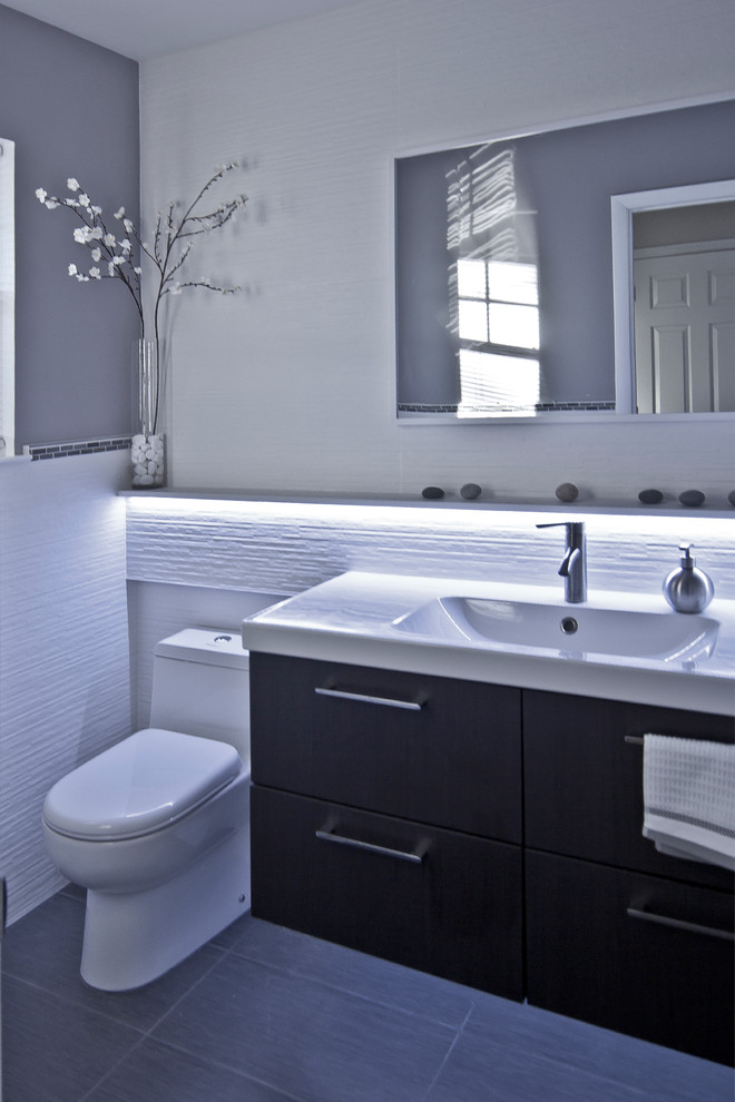 Cette image montre un petit WC et toilettes minimaliste en bois foncé avec un lavabo intégré, un placard à porte plane, WC à poser, un carrelage blanc, des carreaux de céramique, un mur gris et un sol en carrelage de porcelaine.