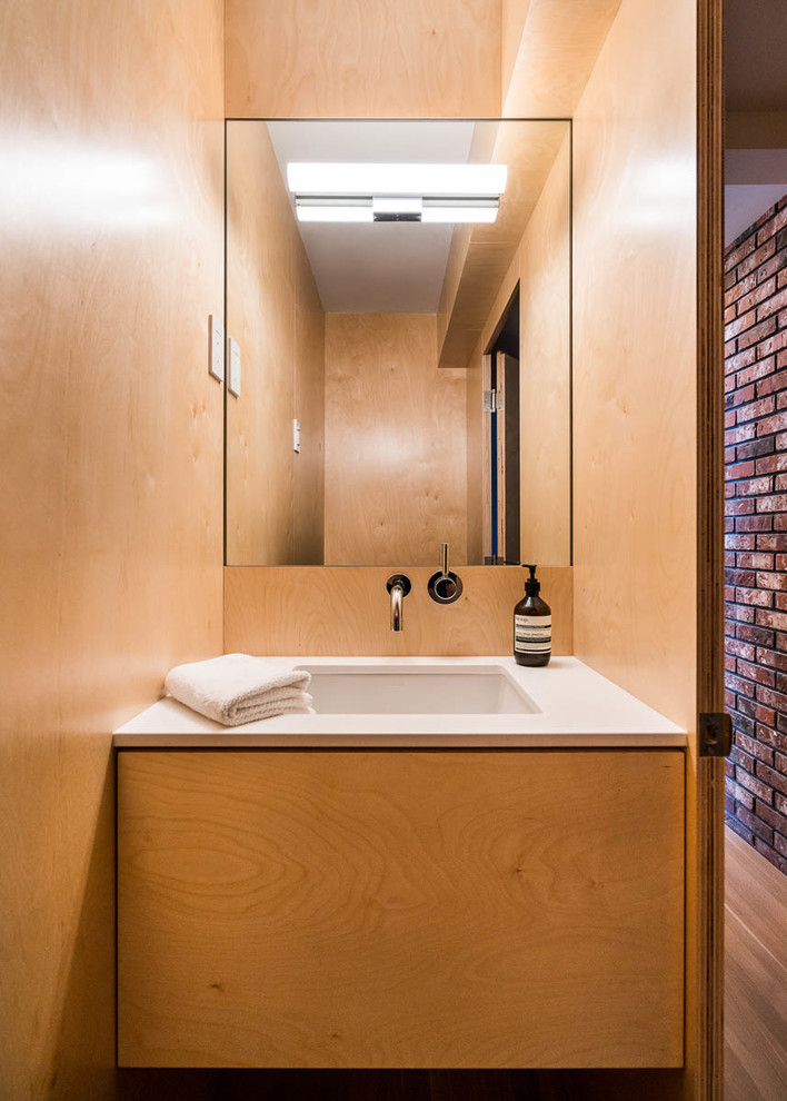 Пример оригинального дизайна: туалет в стиле модернизм с плоскими фасадами, фасадами цвета дерева среднего тона, врезной раковиной и белой столешницей