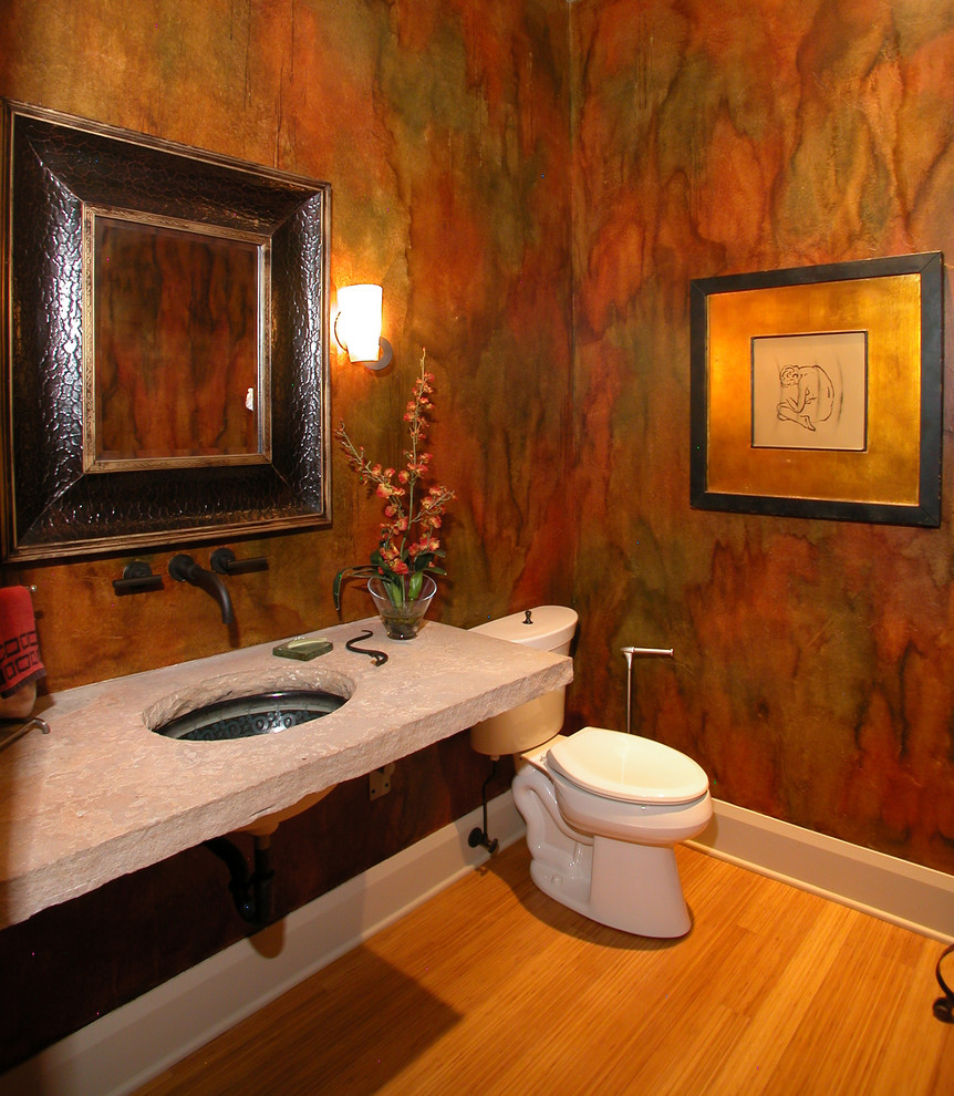 Cette image montre un WC et toilettes design de taille moyenne avec WC séparés, un mur orange, parquet en bambou, un lavabo encastré et un plan de toilette en calcaire.