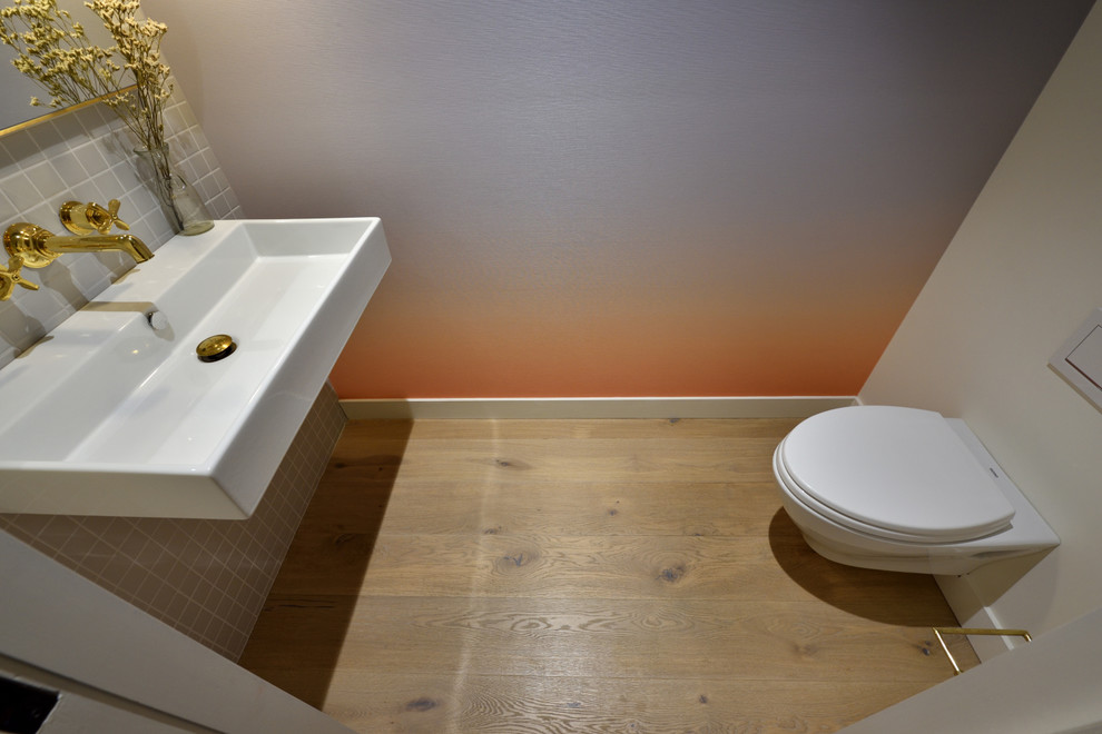 На фото: туалет среднего размера в стиле модернизм с инсталляцией, серой плиткой, керамической плиткой, серыми стенами, светлым паркетным полом, подвесной раковиной, столешницей из искусственного камня и бежевым полом