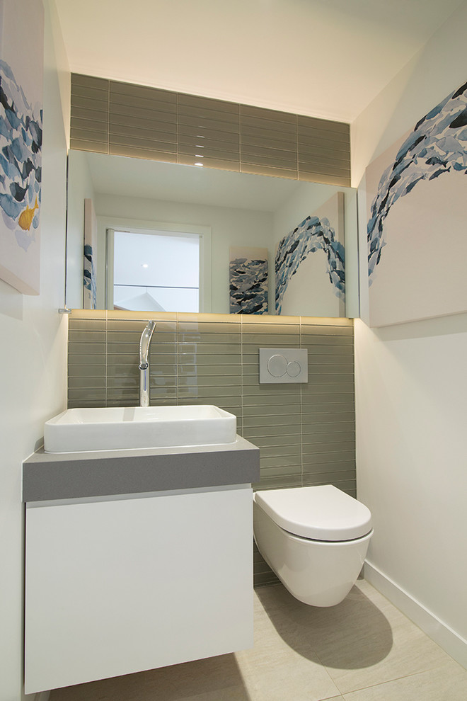 This is an example of a small modern cloakroom in New York with flat-panel cabinets, white cabinets, a bidet, grey tiles, glass tiles, white walls, porcelain flooring, a vessel sink, solid surface worktops, beige floors and grey worktops.