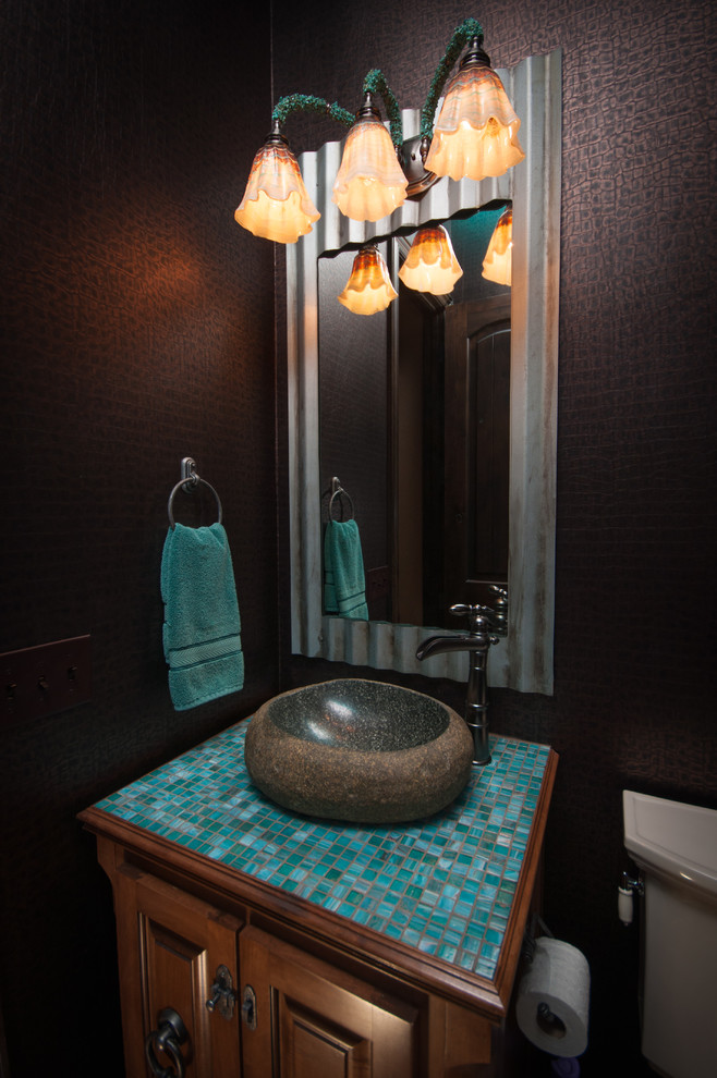 Small eclectic cloakroom in Oklahoma City with a vessel sink, raised-panel cabinets, medium wood cabinets, tiled worktops, blue tiles, glass tiles, brown walls and a two-piece toilet.