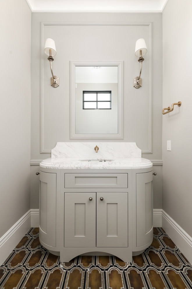 Foto på ett mellanstort funkis grå toalett, med ett integrerad handfat, marmorbänkskiva, brunt golv, luckor med infälld panel, grå skåp och grå väggar