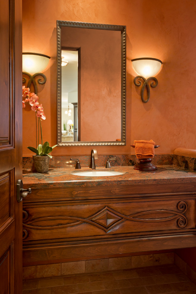 Inspiration för mellanstora medelhavsstil toaletter, med ett undermonterad handfat, möbel-liknande, skåp i mellenmörkt trä, granitbänkskiva, en toalettstol med hel cisternkåpa, orange väggar och travertin golv