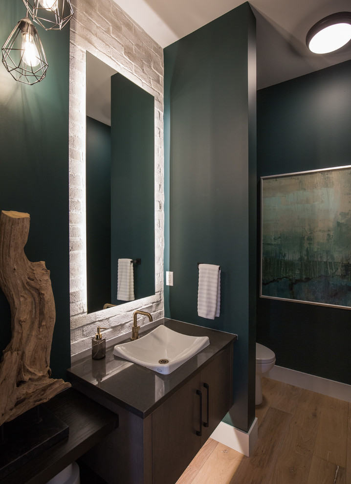 Inspiration for a large contemporary cloakroom in Calgary with flat-panel cabinets, dark wood cabinets, a two-piece toilet, white tiles, stone tiles, green walls, medium hardwood flooring, a vessel sink, engineered stone worktops, brown floors and black worktops.