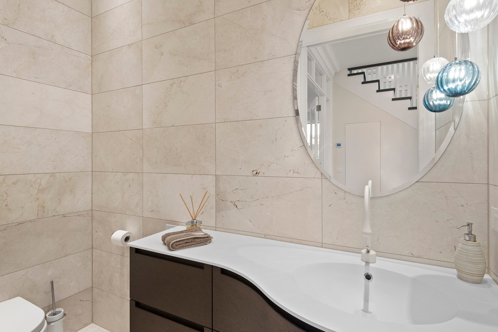 Powder room - large contemporary beige tile and porcelain tile ceramic tile powder room idea in Melbourne with flat-panel cabinets, dark wood cabinets, a wall-mount toilet, beige walls and an integrated sink