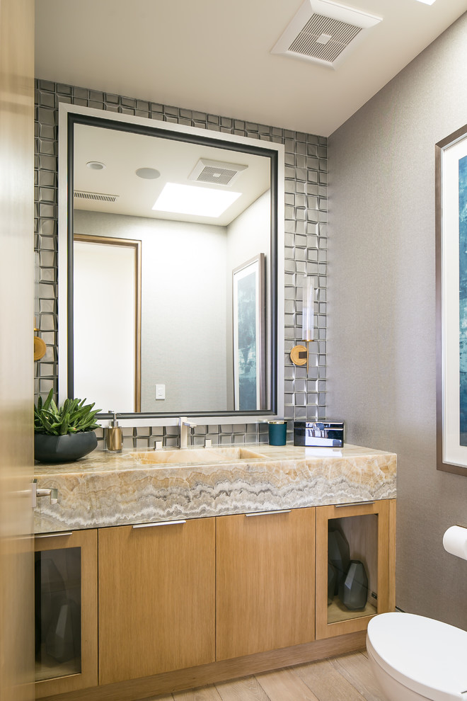 На фото: туалет в современном стиле с плоскими фасадами, фасадами цвета дерева среднего тона, серой плиткой, серыми стенами, светлым паркетным полом, монолитной раковиной, бежевым полом и бежевой столешницей