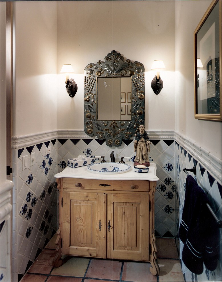 Powder room - mid-sized mediterranean blue tile and ceramic tile terra-cotta tile powder room idea in San Diego with a drop-in sink, furniture-like cabinets, medium tone wood cabinets, marble countertops, a two-piece toilet and white walls