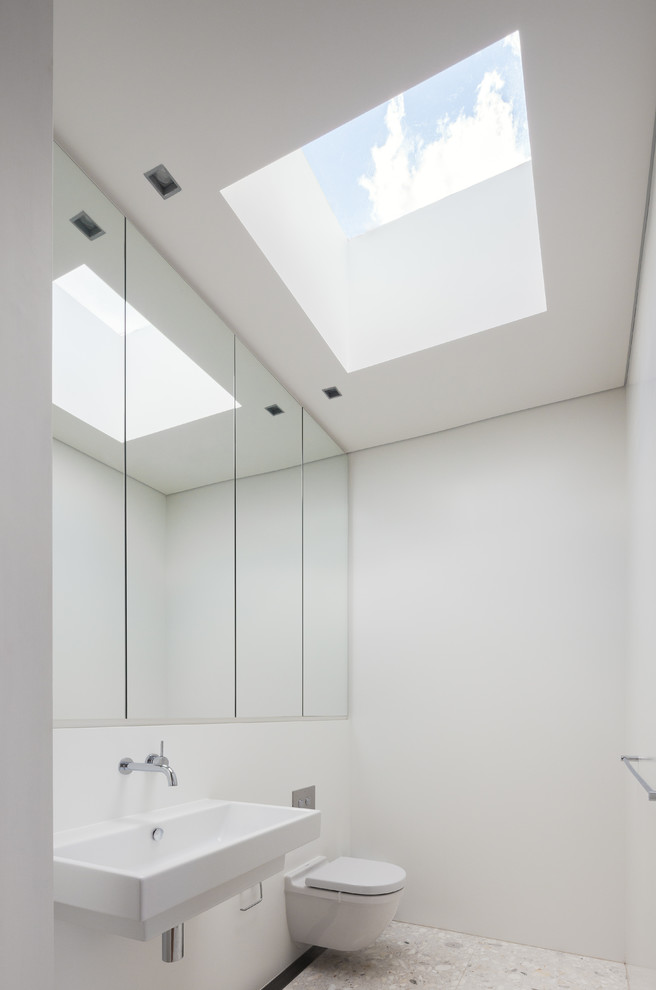 Cette photo montre un WC suspendu moderne avec un mur blanc, un lavabo suspendu et un sol blanc.