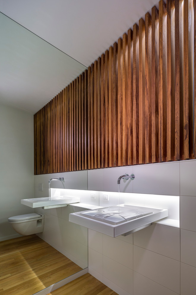 Foto di un bagno di servizio moderno con lavabo sospeso, WC sospeso, piastrelle bianche, piastrelle in ceramica e pavimento in legno massello medio