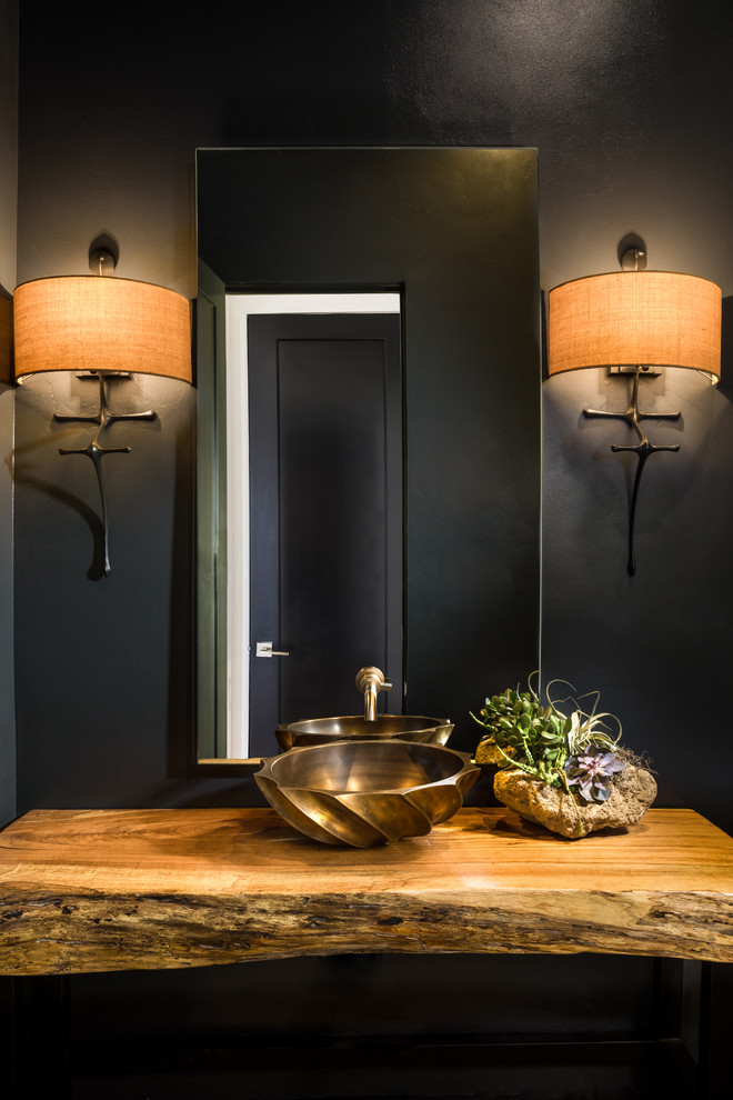 Imagen de aseo contemporáneo con paredes negras, lavabo sobreencimera y encimera de madera