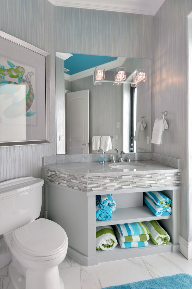 Cette photo montre un WC et toilettes tendance avec un placard sans porte, des portes de placard grises, un carrelage gris, un lavabo encastré, un mur gris et un sol en marbre.