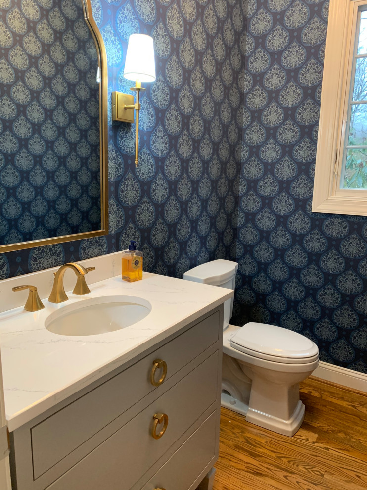 Example of a small classic medium tone wood floor and brown floor powder room design in Philadelphia with flat-panel cabinets, gray cabinets, a two-piece toilet, blue walls, an undermount sink, marble countertops and white countertops