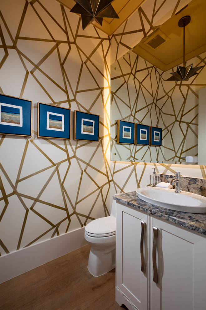 Cette photo montre un WC et toilettes bord de mer avec un placard avec porte à panneau encastré, des portes de placard blanches, un mur multicolore, un sol en bois brun, une vasque et un plan de toilette multicolore.