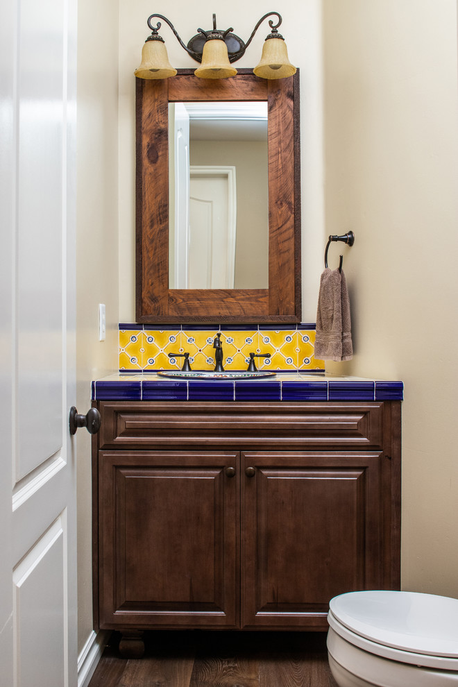 This is an example of a small cloakroom in San Diego with raised-panel cabinets, brown cabinets, a two-piece toilet, ceramic tiles, beige walls, dark hardwood flooring, a built-in sink, tiled worktops, brown floors and blue worktops.