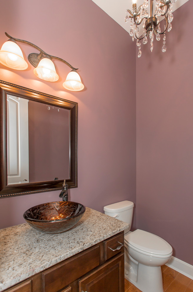 Klassische Gästetoilette mit Schrankfronten mit vertiefter Füllung, dunklen Holzschränken, Toilette mit Aufsatzspülkasten, lila Wandfarbe, braunem Holzboden, Aufsatzwaschbecken und Granit-Waschbecken/Waschtisch in Cincinnati