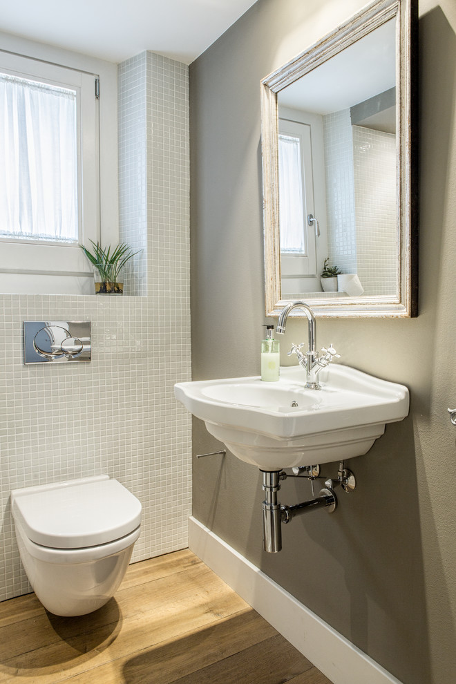Photo of a small classic cloakroom in Other with a wall mounted toilet, medium hardwood flooring, a wall-mounted sink, grey tiles and grey walls.