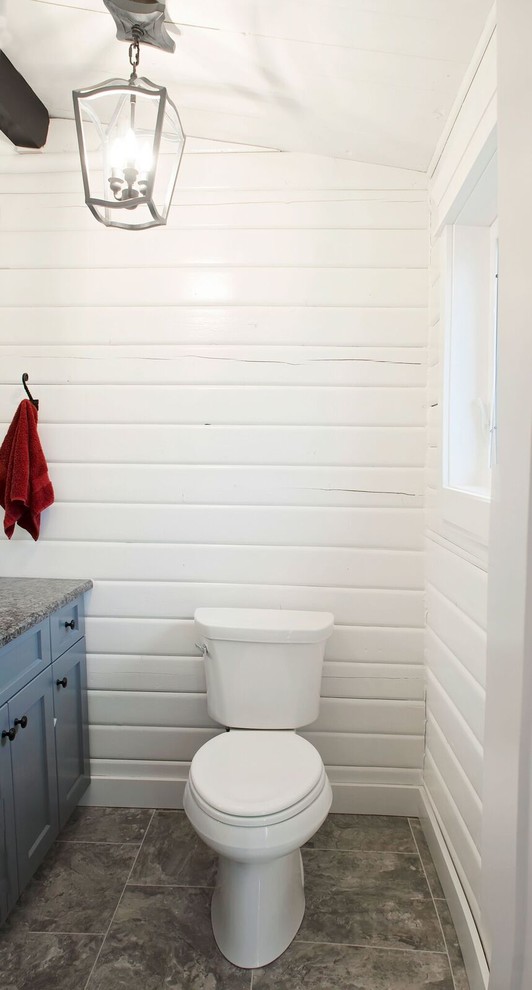 Idée de décoration pour un WC et toilettes champêtre de taille moyenne avec un placard à porte shaker, des portes de placard bleues, WC séparés, un mur blanc, un sol en carrelage de céramique, un lavabo encastré, un plan de toilette en granite et un sol marron.