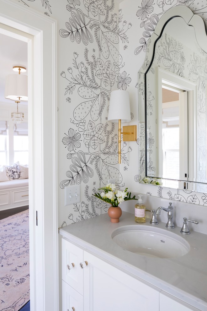 Klassisk inredning av ett litet grå grått toalett, med luckor med infälld panel, vita skåp, ett undermonterad handfat, vita väggar och granitbänkskiva