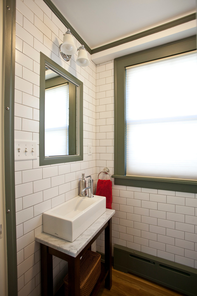Klassische Gästetoilette mit Aufsatzwaschbecken, verzierten Schränken, dunklen Holzschränken, weißen Fliesen, Metrofliesen, braunem Holzboden und weißer Waschtischplatte in Minneapolis