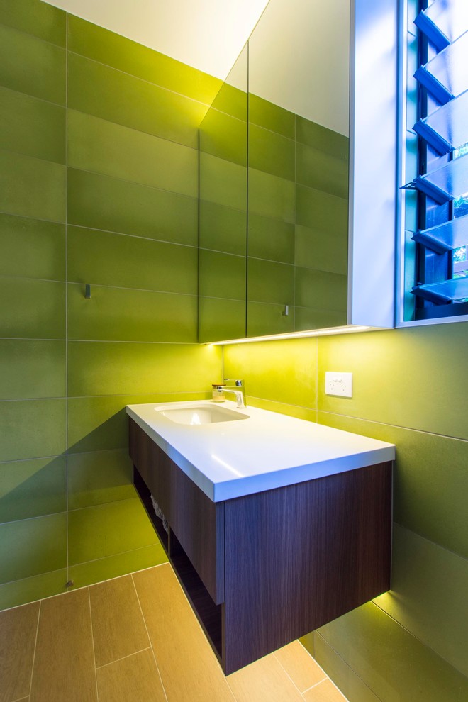 На фото: туалет среднего размера с унитазом-моноблоком, зеленой плиткой, керамической плиткой, зелеными стенами, светлым паркетным полом, врезной раковиной и столешницей из искусственного кварца