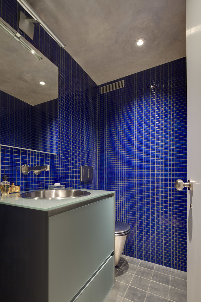 На фото: маленький туалет в современном стиле с накладной раковиной, плоскими фасадами, серыми фасадами, стеклянной столешницей, синей плиткой, плиткой мозаикой и синими стенами для на участке и в саду с