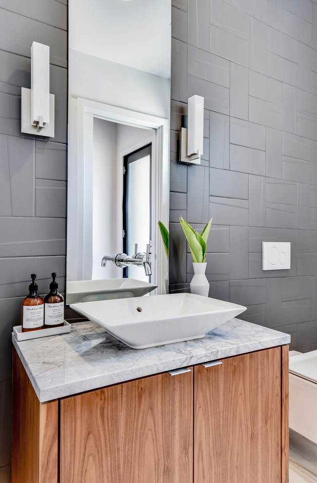 Cette image montre un WC suspendu design en bois brun avec un placard à porte plane, un carrelage gris, un mur gris, une vasque, un plan de toilette en marbre et un plan de toilette gris.