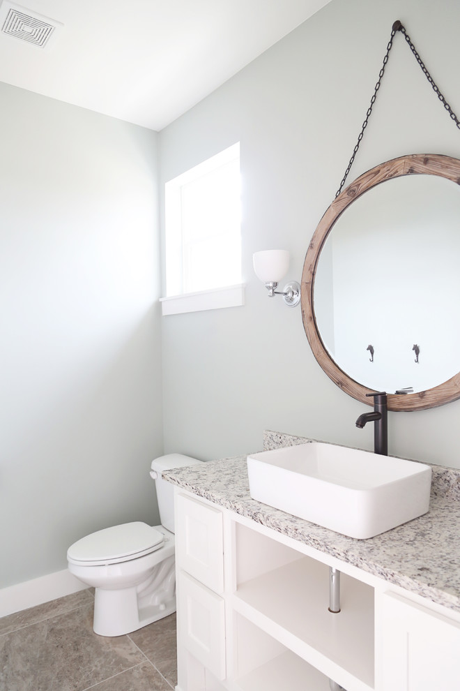 Mid-sized farmhouse ceramic tile and beige floor powder room photo in Other with furniture-like cabinets, white cabinets, a two-piece toilet, blue walls, a vessel sink, granite countertops and gray countertops