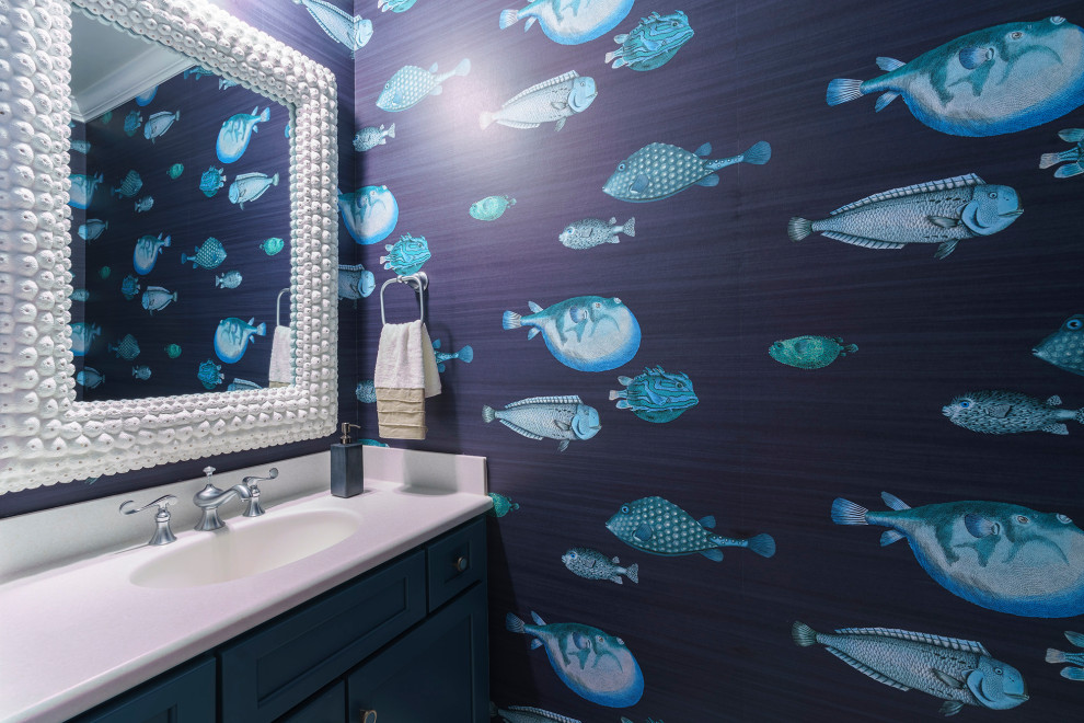 Cette photo montre un WC et toilettes bord de mer avec un placard à porte shaker, des portes de placard bleues, un mur bleu, un lavabo intégré, un plan de toilette blanc, meuble-lavabo encastré et du papier peint.