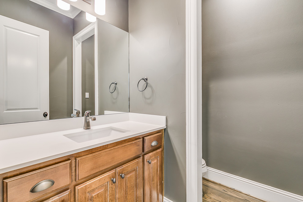 Inspiration for a small classic cloakroom in Dallas with raised-panel cabinets, medium wood cabinets, a one-piece toilet, grey walls, medium hardwood flooring, a built-in sink and quartz worktops.