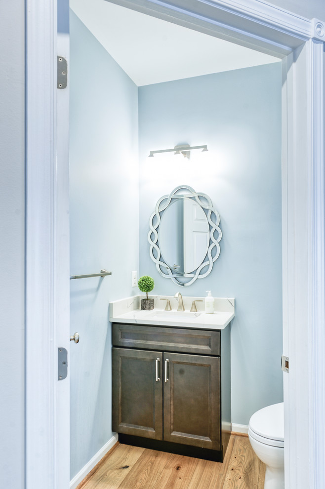 Inspiration for a small transitional light wood floor and brown floor powder room remodel in DC Metro with beaded inset cabinets, distressed cabinets, a two-piece toilet, blue walls, an undermount sink, quartzite countertops and white countertops