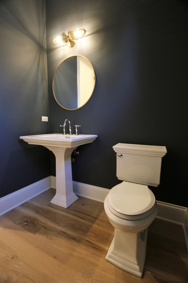 Photo of a small classic cloakroom in Chicago with a two-piece toilet, black walls, light hardwood flooring, a pedestal sink and beige floors.