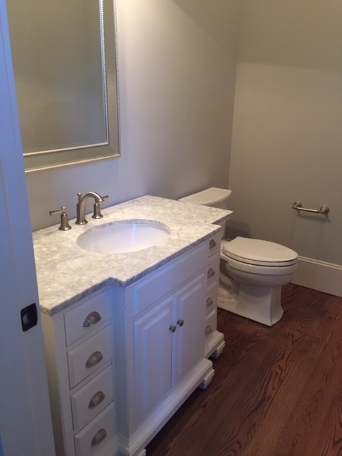 Foto på ett mellanstort vintage toalett, med vita skåp, en toalettstol med separat cisternkåpa, grå väggar, ett undermonterad handfat, marmorbänkskiva, luckor med upphöjd panel och mörkt trägolv